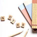 five brown wooden scrabble tiles beside two pencils